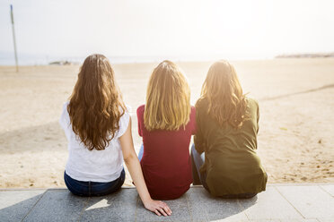 Rear view of three female friends sitting at the beach - GIOF03007