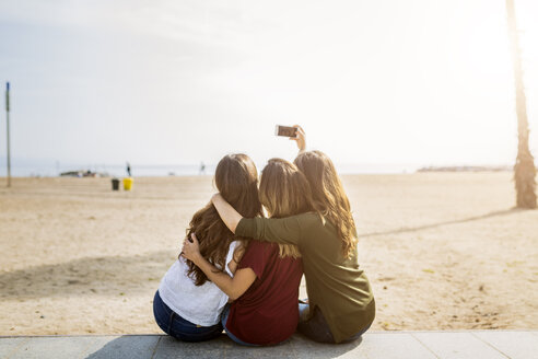 Rückansicht von drei Freundinnen, die am Strand sitzen und ein Selfie machen - GIOF03008