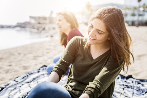 Zwei glückliche junge Frauen sitzen am Strand - GIOF03012