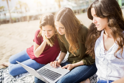 Drei Freundinnen benutzen einen Laptop am Strand, lizenzfreies Stockfoto