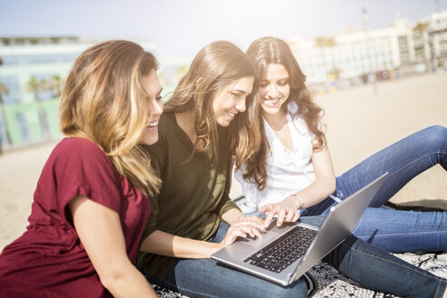 Drei glückliche Freundinnen benutzen einen Laptop am Strand - GIOF03017