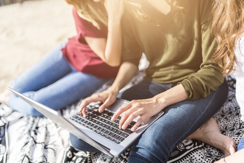 Zwei Frauen benutzen einen Laptop am Strand - GIOF03019