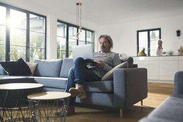 Senior man sitting on couch, using laptop - SBOF00457