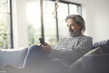 Älterer Mann sitzt auf der Couch und benutzt sein Smartphone - SBOF00461