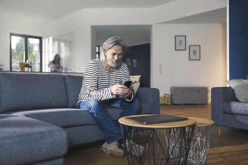 Älterer Mann sitzt auf der Couch und benutzt sein Smartphone - SBOF00464