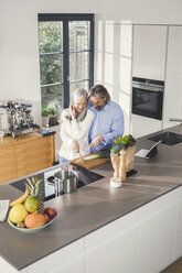 Glückliches älteres Paar bei der Zubereitung von Speisen in der Küche mit Online-Rezept - SBOF00495