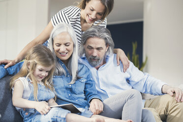 Family sitting on couch, watching granddaughter use tablet pc - SBOF00528