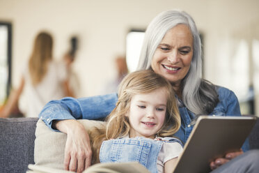 Grandmother and granddaughter sitting on couch, reading together - SBOF00536