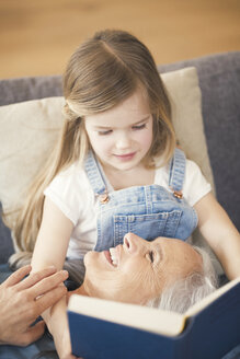 Großmutter und Enkelin sitzen auf der Couch und lesen gemeinsam ein Buch - SBOF00537