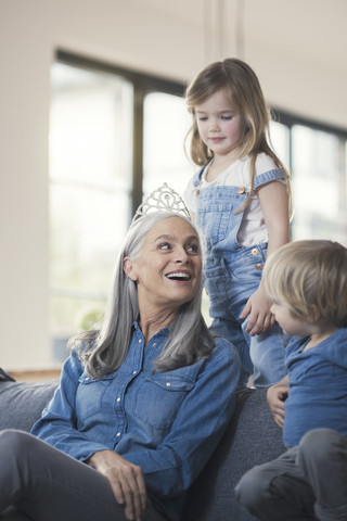 Großmutter mit Krone, sitzend auf der Couch mit Enkelkindern, lizenzfreies Stockfoto
