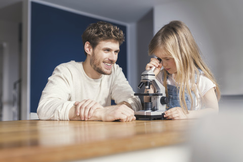 Vater beobachtet Tochter bei der Benutzung eines Mikroskops und lächelt stolz, lizenzfreies Stockfoto