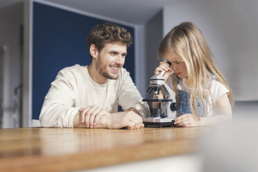 Father watching daughter use a microscope, smiling proudly - SBOF00544