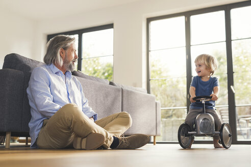 Grandfather playing with grandson, sitting on toy car - SBOF00552