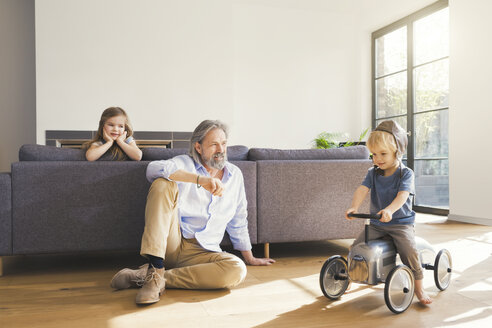 Großvater spielt mit Enkelkindern, sitzt auf Spielzeugauto - SBOF00554