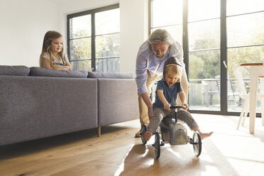 Grandfather playing with grandchildren, sitting on toy car - SBOF00556