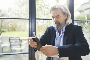 Senior businessman sitting on chair, using smartphone - SBOF00562