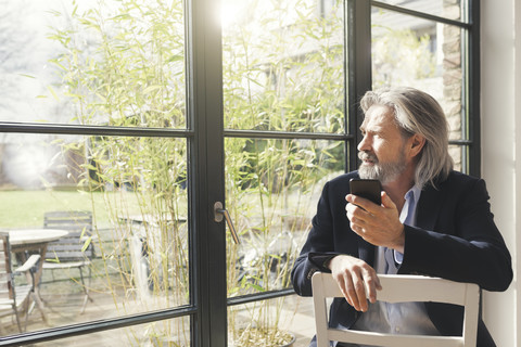 Älterer Geschäftsmann sitzt auf einem Stuhl und benutzt ein Smartphone, lizenzfreies Stockfoto