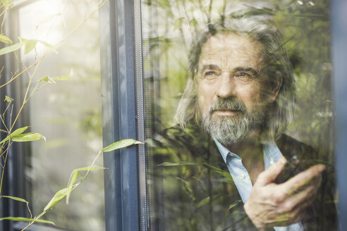 Senior businessman standing by window, using smartphone - SBOF00566