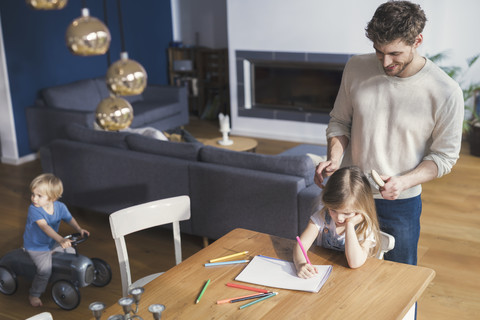 Vater bürstet die Haare seiner Tochter, während sie malt, lizenzfreies Stockfoto