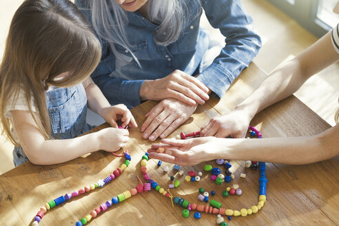 Grandmother and granddaughter and mother threading beads - SBOF00578