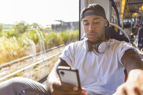 Porträt eines jungen Mannes in der Straßenbahn, der auf sein Smartphone schaut - MGIF00068