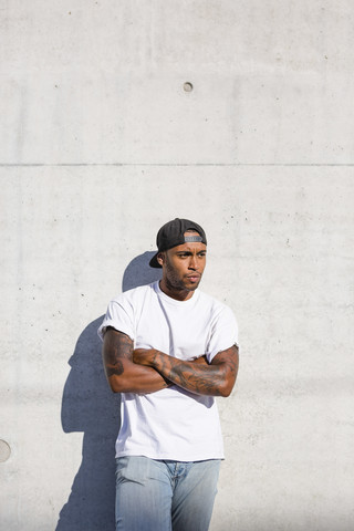 Portrait of angry young man with arms crossed standing in front of concrete wall stock photo