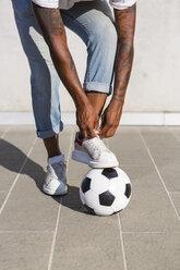 Young man tying his shoes on a soccer ball, partial view - MGIF00076