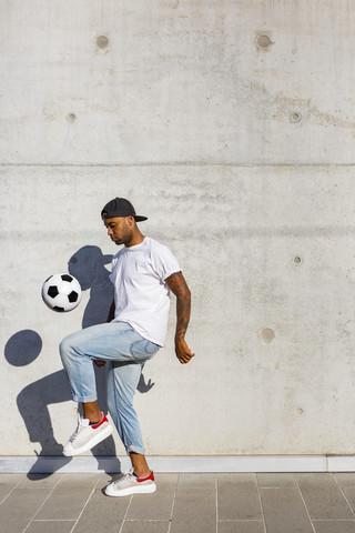 Junger Mann spielt mit Fußball vor einer Betonmauer, lizenzfreies Stockfoto