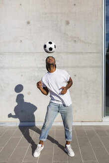 Junger Mann spielt mit Fußball vor einer Betonmauer - MGIF00078