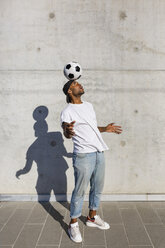 Junger Mann balanciert Fußball auf seinem Kopf vor einer Betonwand - MGIF00079