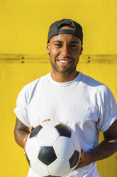 Porträt eines lächelnden Mannes mit Fußball vor einer gelben Wand - MGIF00081