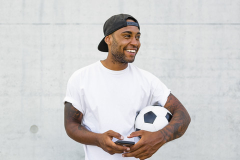 Porträt eines lachenden jungen Mannes mit Fußball und Mobiltelefon, lizenzfreies Stockfoto