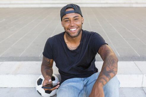 Porträt eines lachenden jungen Mannes mit Smartphone - MGIF00091