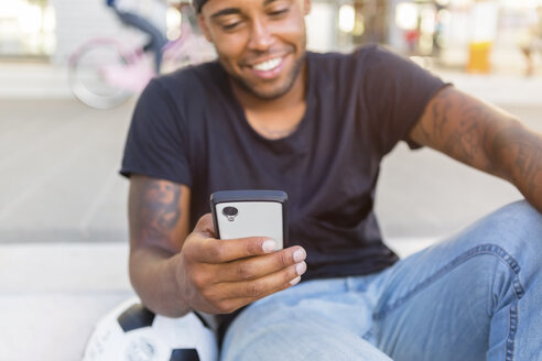 Lächelnder junger Mann schaut auf sein Smartphone, Nahaufnahme - MGIF00092