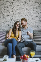 Laughing couple sitting on couch watching TV - MOMF00204