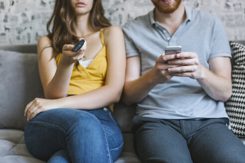 Couple sitting on couch with remote control and smartphone, partial view - MOMF00205