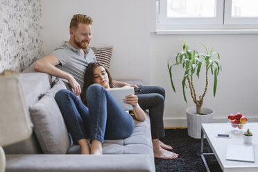 Couple on the sofa in the living room using tablet - MOMF00212