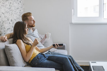 Ehepaar sitzt auf der Couch, trinkt Kaffee und sieht fern - MOMF00215