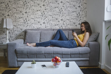 Frau auf Couch im Wohnzimmer beim Lesen eines E-Books - MOMF00216
