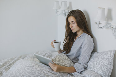 Frau benutzt Tablet, während sie morgens im Bett Kaffee trinkt - MOMF00218