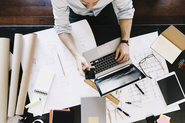 Mann mit Laptop neben einem Bauplan am Schreibtisch, Draufsicht - GIOF03051