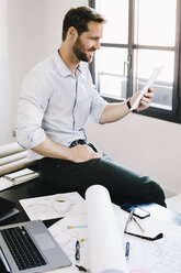 Architect sitting on desk in his office using tablet - GIOF03062