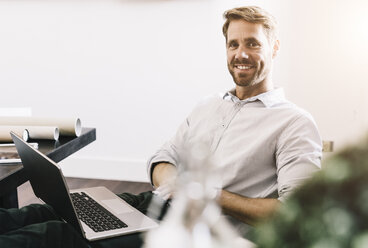 Porträt eines lächelnden Architekten mit Laptop in seinem Büro - GIOF03067