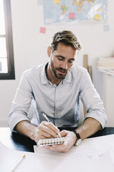 Portrait of architect sitting at desk taking notes - GIOF03072