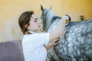 Young woman grooming horse - KIJF01698