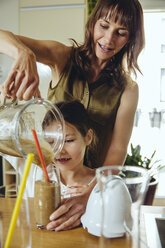 Girl pouring smoothie into glass with mother’s help - MFF03698