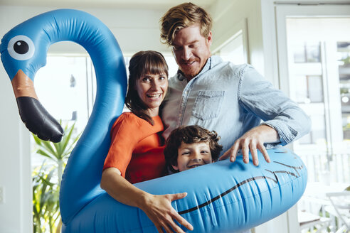 Happy parents with son holding an inflatable flamingo at home - MFF03710