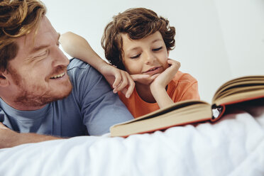 Father and son reading book in bed - MFF03711