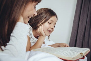 Mother and daughter reading book in bed - MFF03717