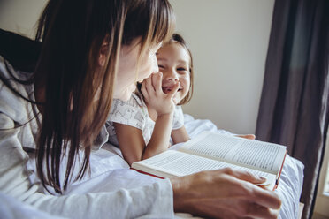 Mother and daughter reading book in bed - MFF03720